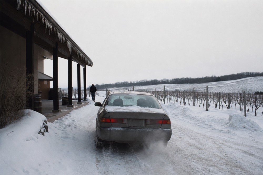 A car parked beside a vineyard with a sign for a winery entrance, no text, no logos, no people