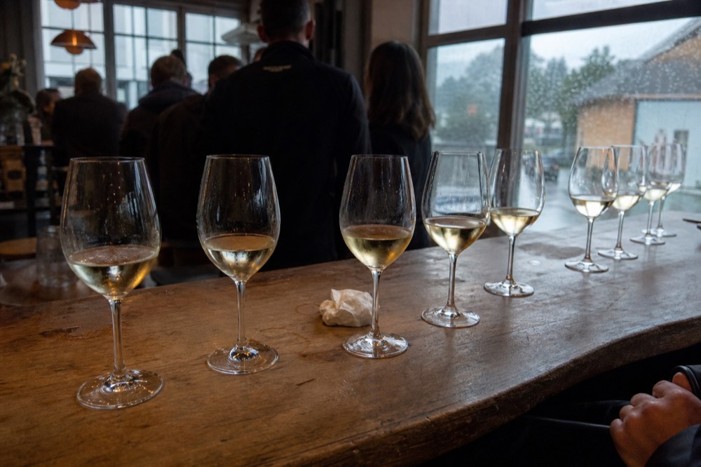 A flight of white wine glasses on a wooden tasting room bar, no text, no logos, no people