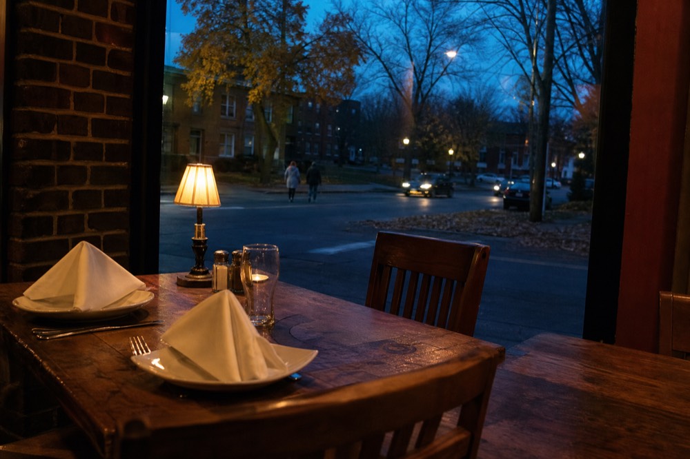 A small-town restaurant table set for dinner beside a window at dusk, no text, no logos, no people