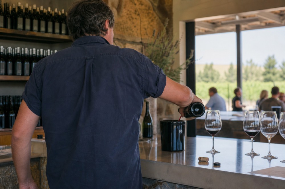 A winemaker pouring wine behind a tasting room bar, no text, no logos, no people