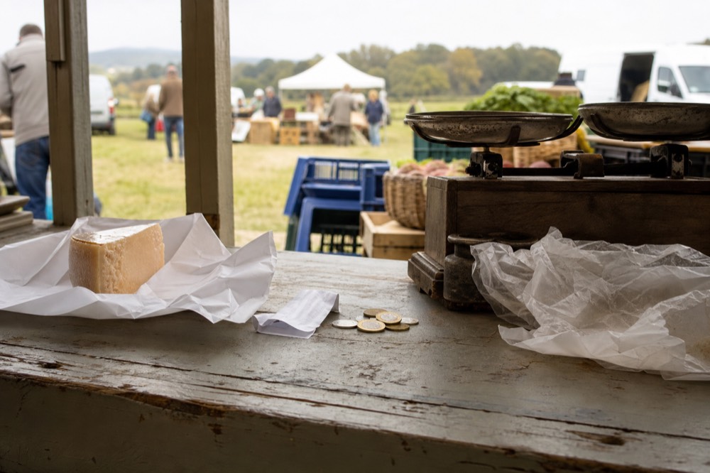 A receipt and coins on a farm market table beside a bag of cheese, no text, no logos, no people
