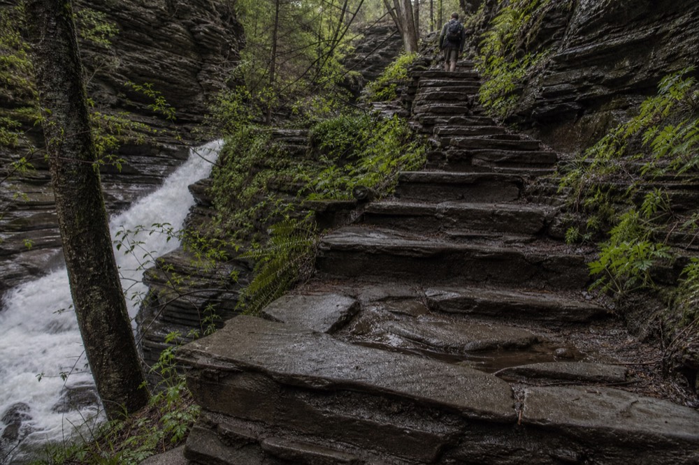 Stone stairway winding beside a waterfall inside a narrow gorge, no text, no logos, no people