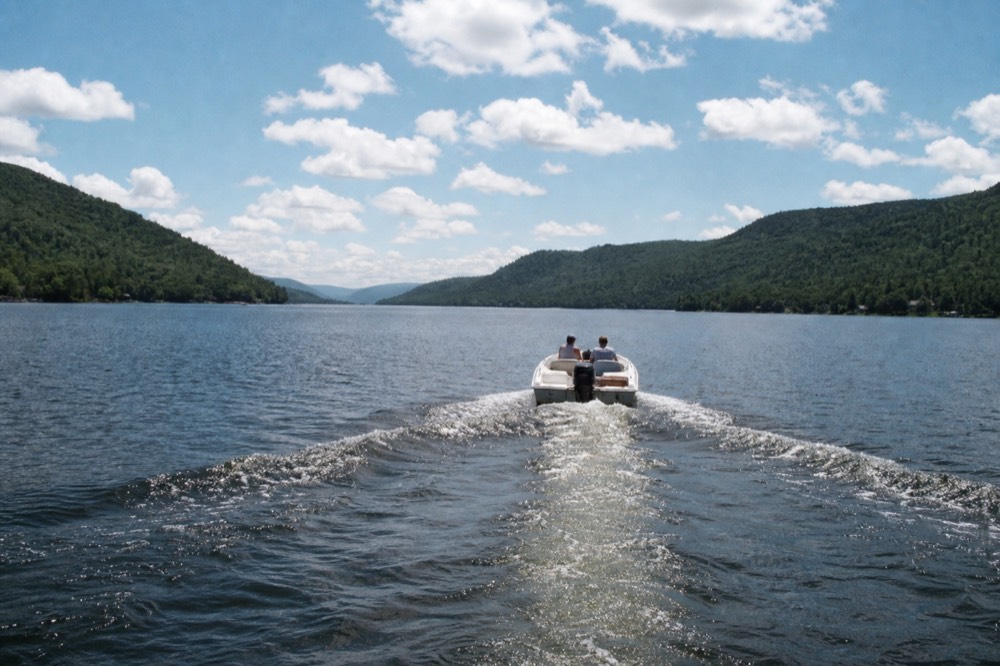Small boat cruising on a long lake with forested hills on both shores, no text, no logos, no people