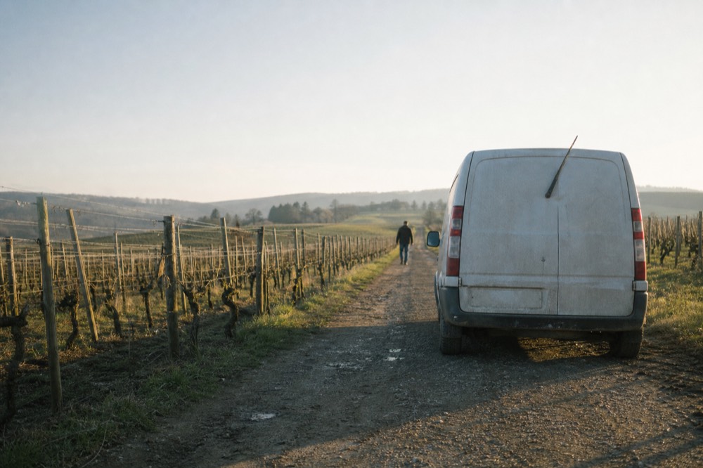 A small van parked on a winery lane between rows of vines, no text, no logos, no people.